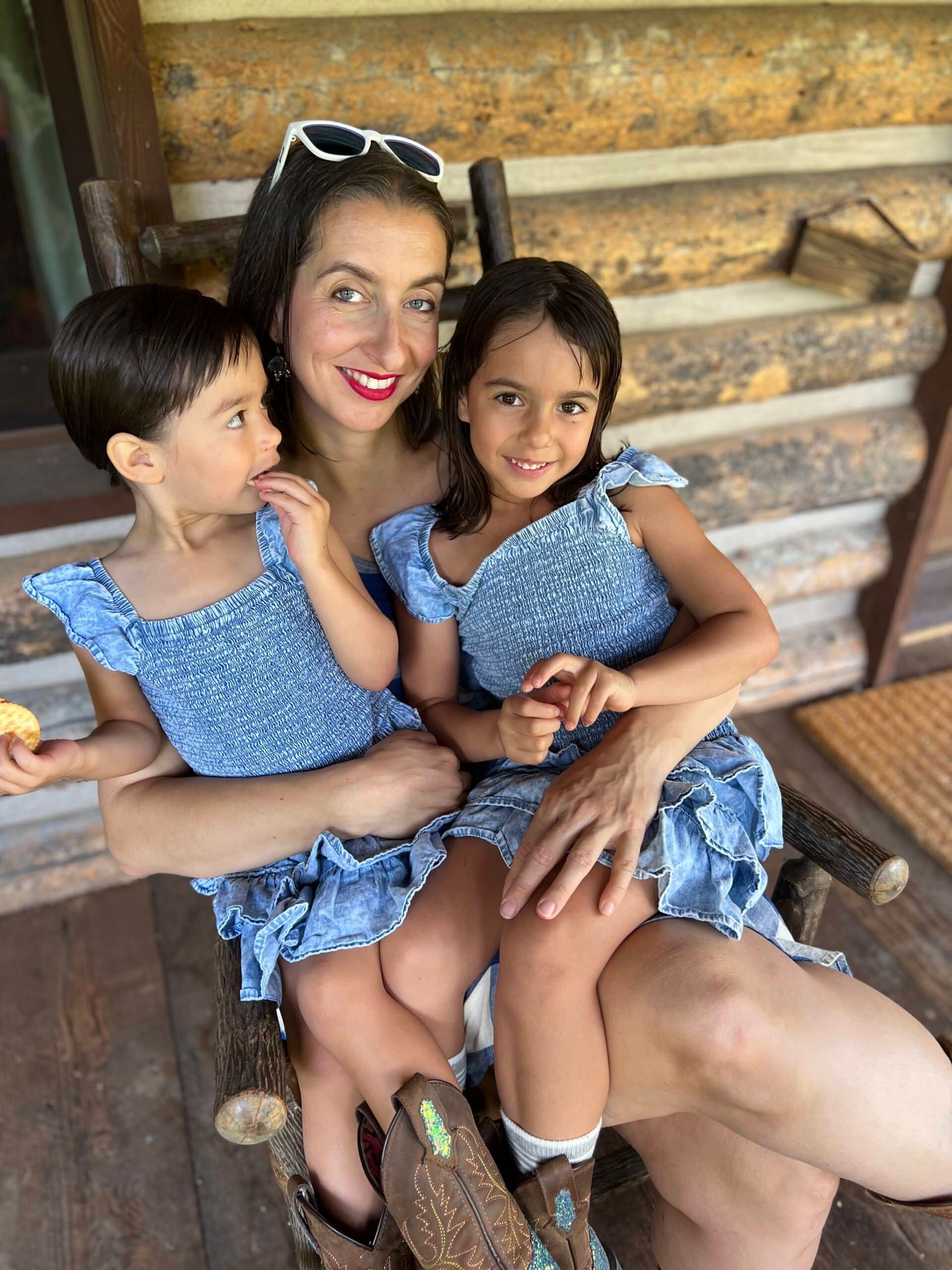 A woman and two children in a rockingchair on the front porch or a rustic cabin