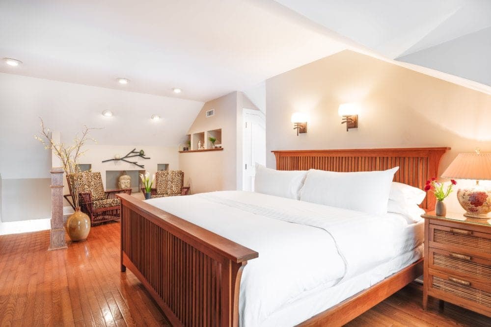 Modern wood bed with white coverings, nightstand and 2 chairs in sitting area