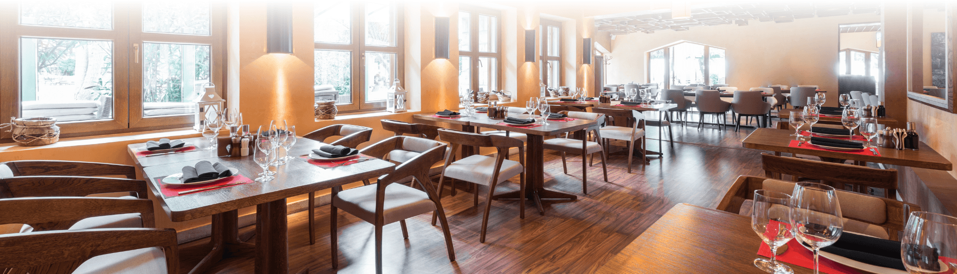 A restaurant with man tables, chairs, and windows depicting a bright day