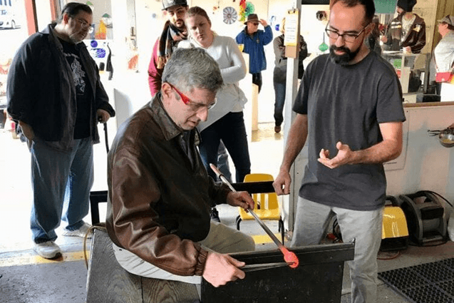 Man blowing glass outdoors with spectators watching