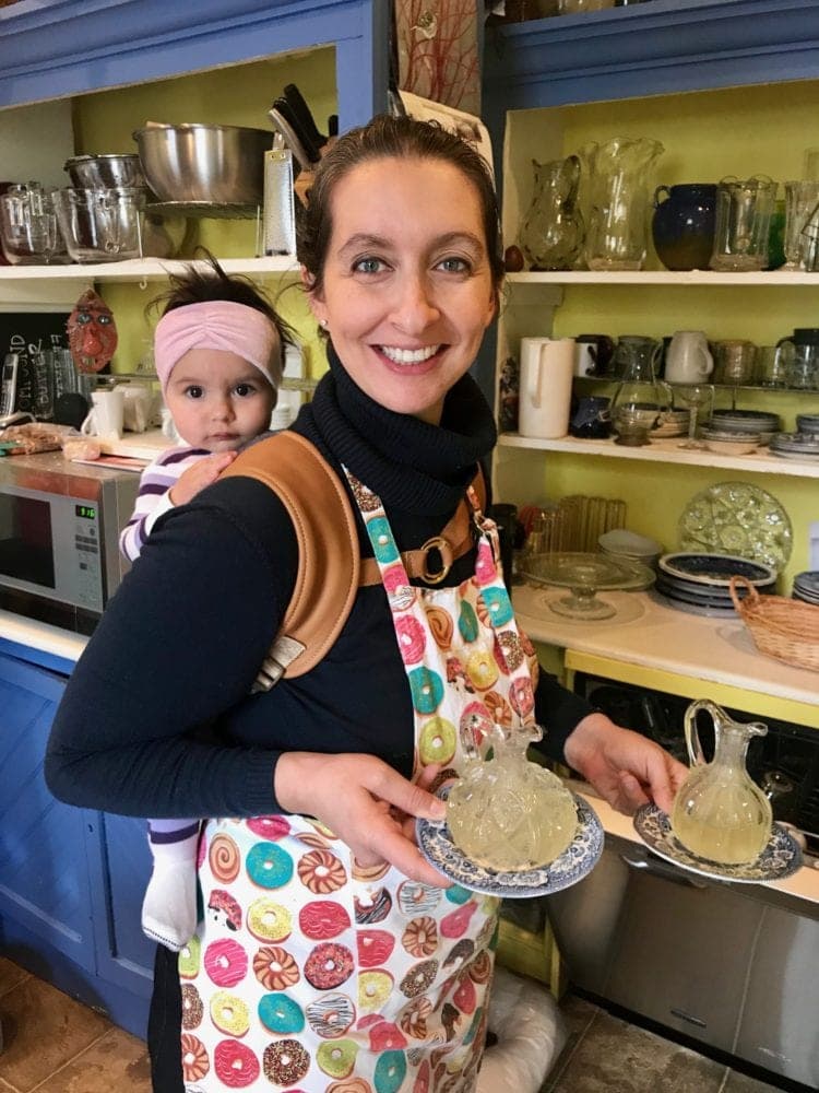 Woman holding a baby while carrying a tray of tea